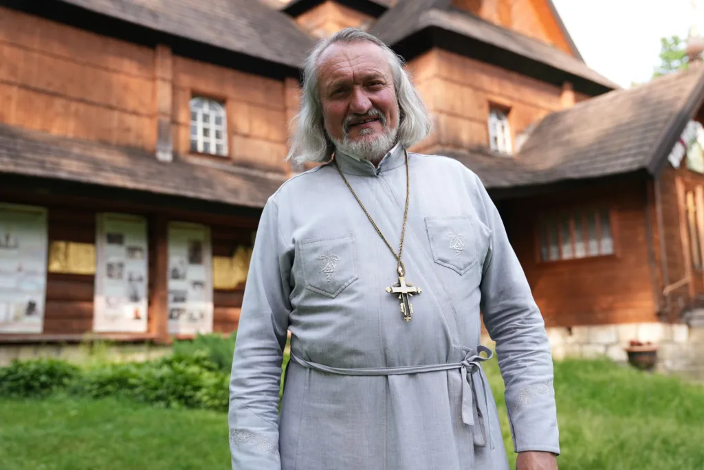 Священник стоїть перед дерев’яною церквою