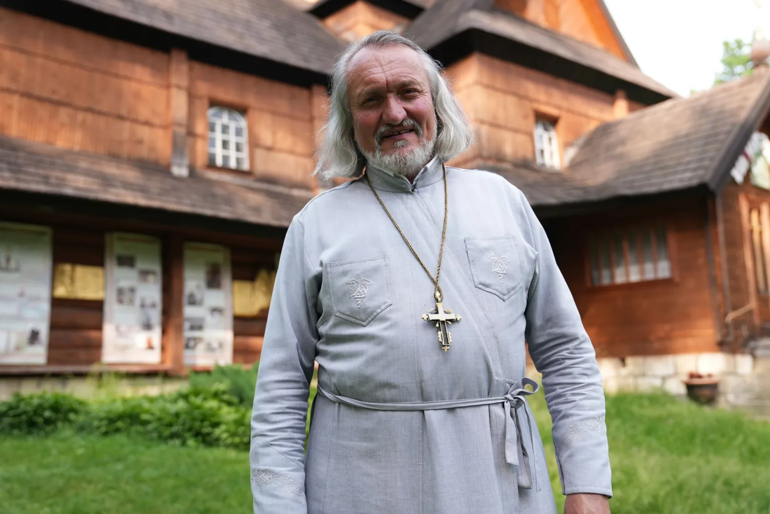 Священник стоїть перед дерев’яною церквою