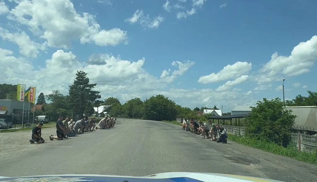 Люди стоять на колінах обабіч дороги