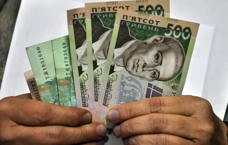 Людина тримає українські гривні в руках