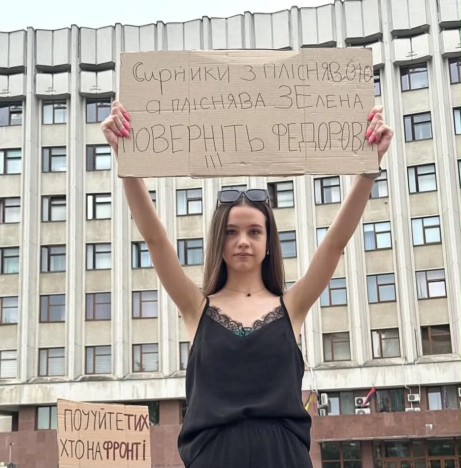 Жінка тримає протестний плакат перед будівлею