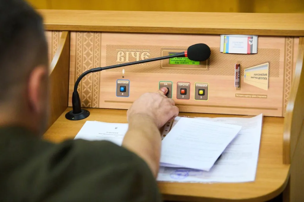 Депутат натискає кнопку для голосування у сесійній залі