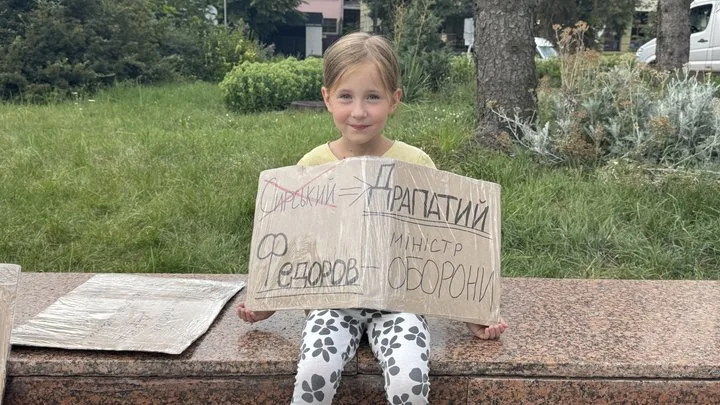 Дівчинка тримає картонний плакат на вулиці