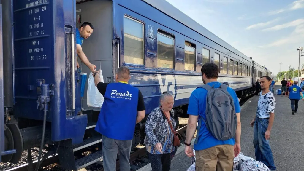 Волонтери допомагають пасажирам біля синього потяга