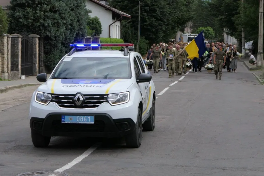 Поліцейський автомобіль перед колоною з прапором України