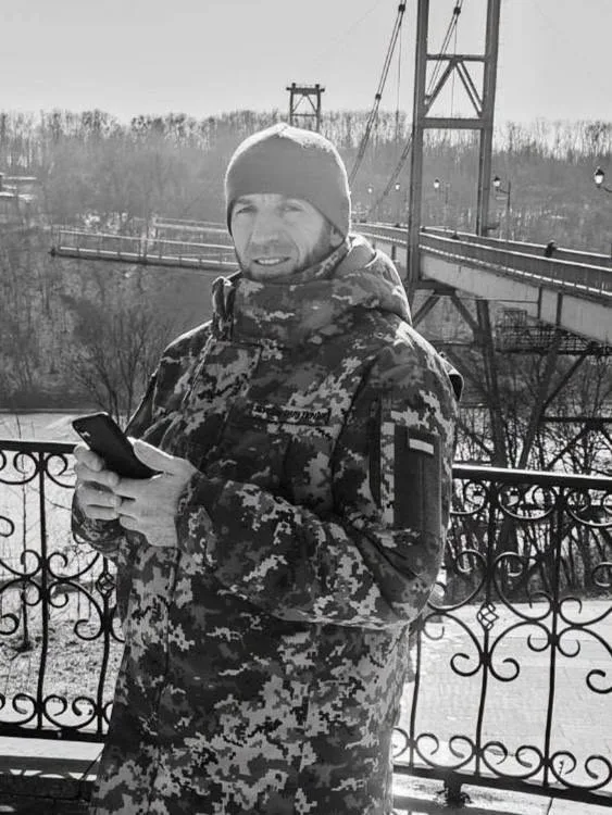 Чоловік у камуфляжі стоїть біля мосту взимку