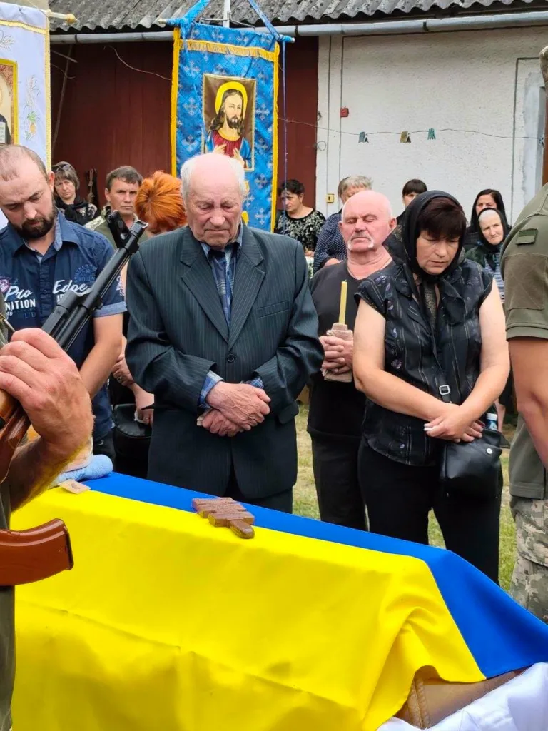 Люди моляться біля труни, накритої прапором України