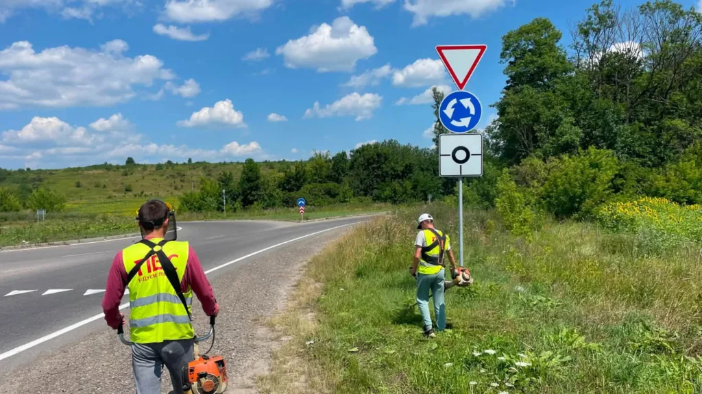 Робітники косять траву біля дороги на перехресті