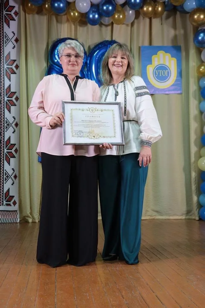 Дві жінки тримають грамоту на святковій сцені
