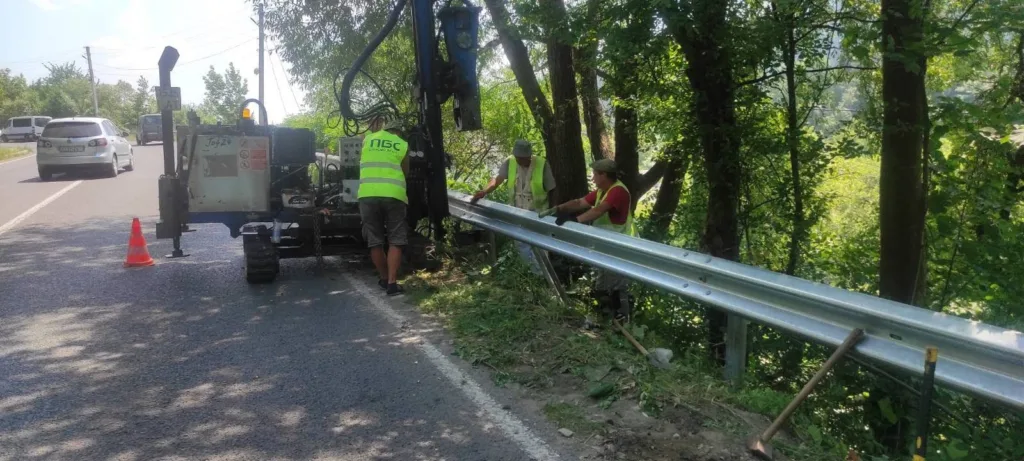 Робітники встановлюють дорожнє огородження біля лісу