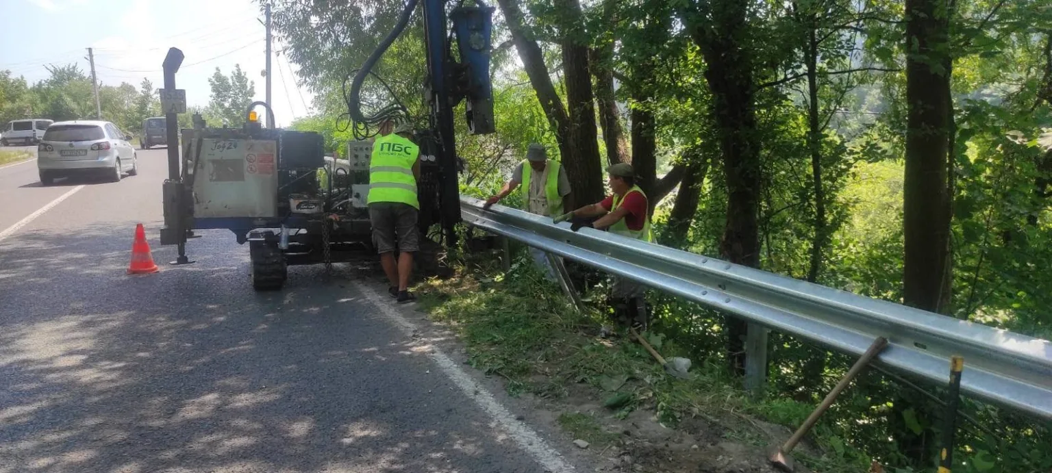 Робітники встановлюють дорожнє огородження біля лісу