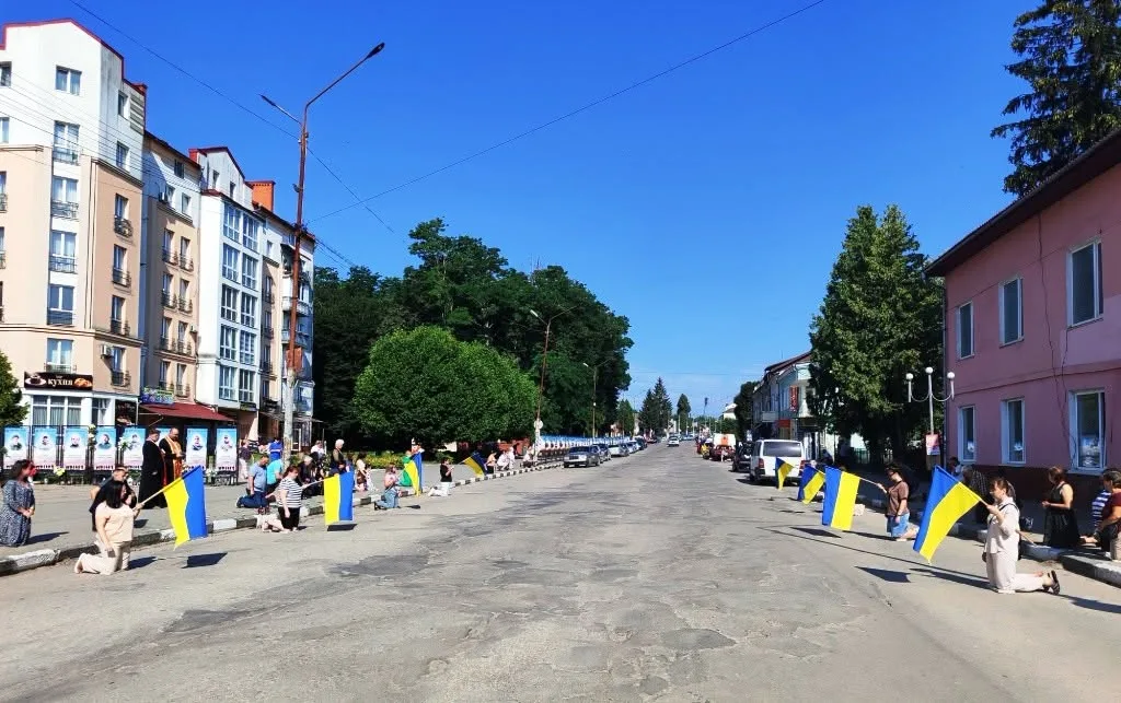 Люди з українськими прапорами стоять уздовж вулиці