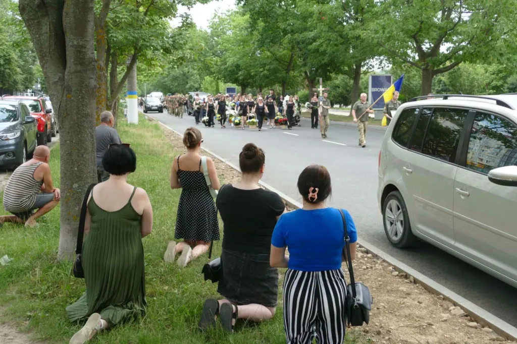 Люди на колінах під час військової процесії