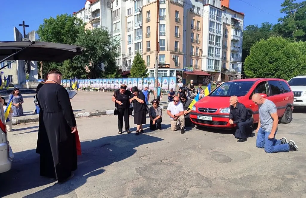 Люди стоять і моляться біля червоного автомобіля
