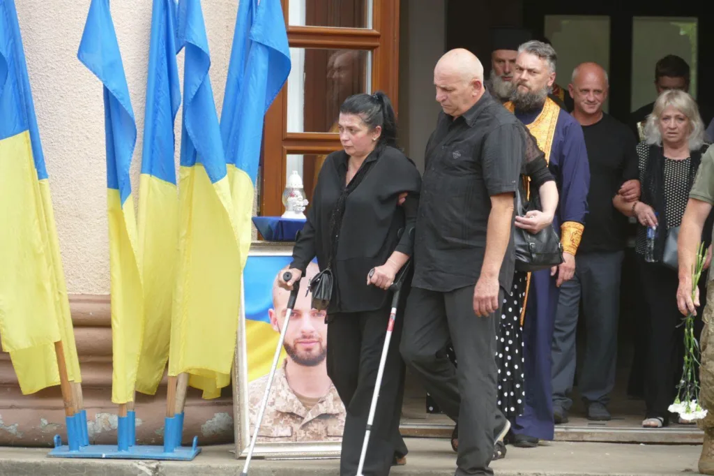 Люди виходять із жалобної церемонії під прапорами України
