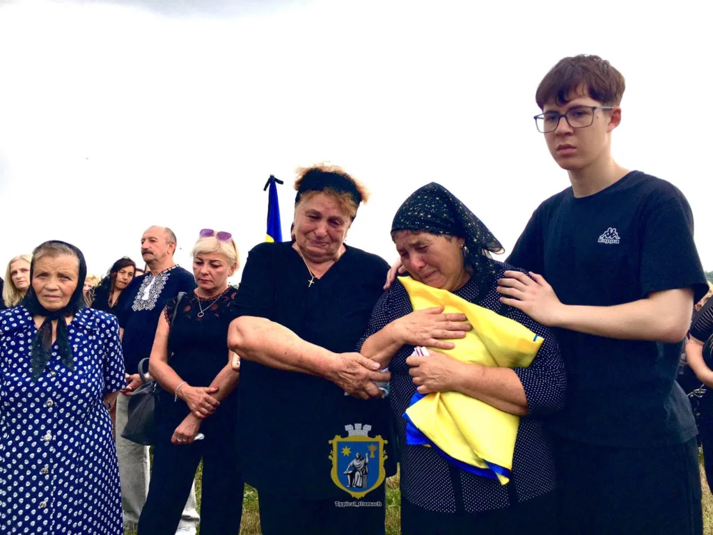 Люди сумують, тримаючи український прапор.