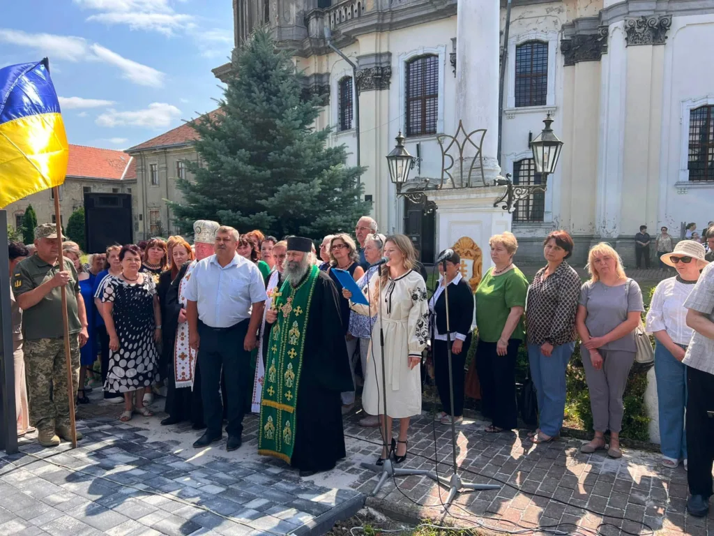 Люди на урочистому заході біля церкви з прапором