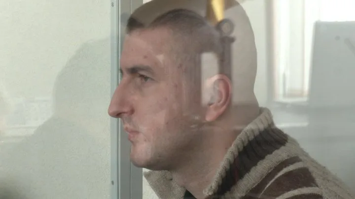 Чоловік у скляній кабіні під час судового засідання