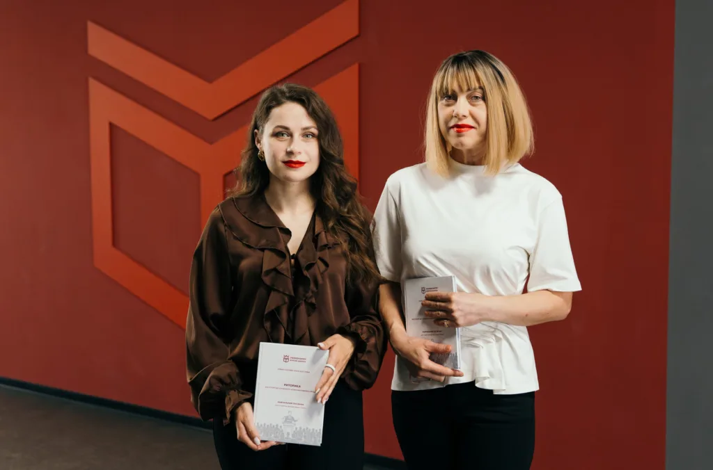 Дві жінки з книгами біля червоної стіни