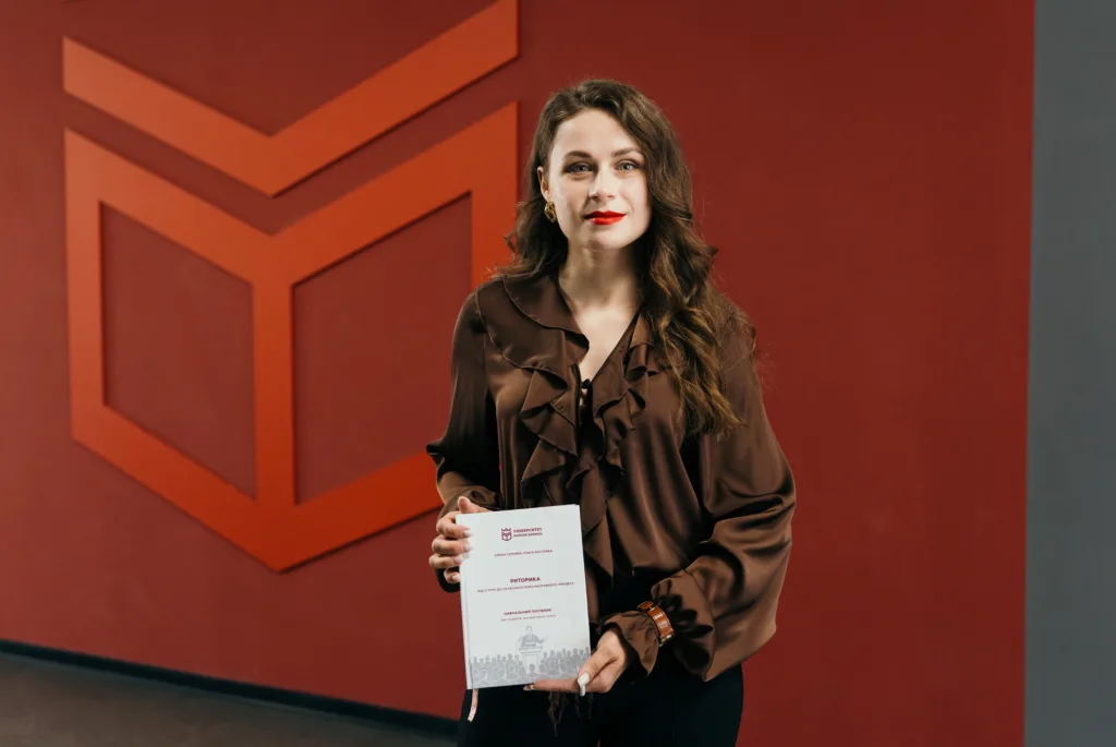 Жінка тримає книгу перед червоною стіною