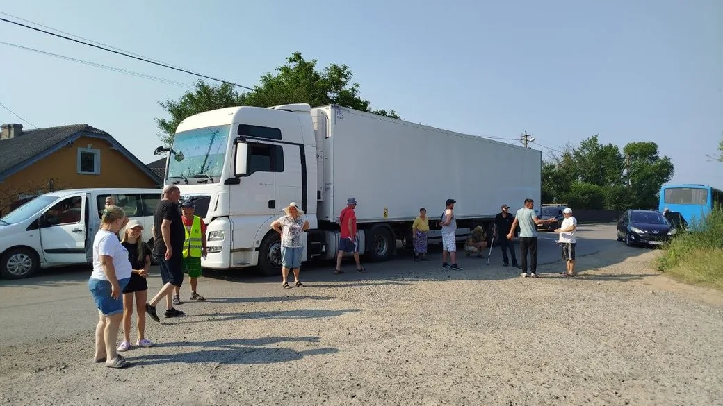 Люди біля великої білої вантажівки на дорозі