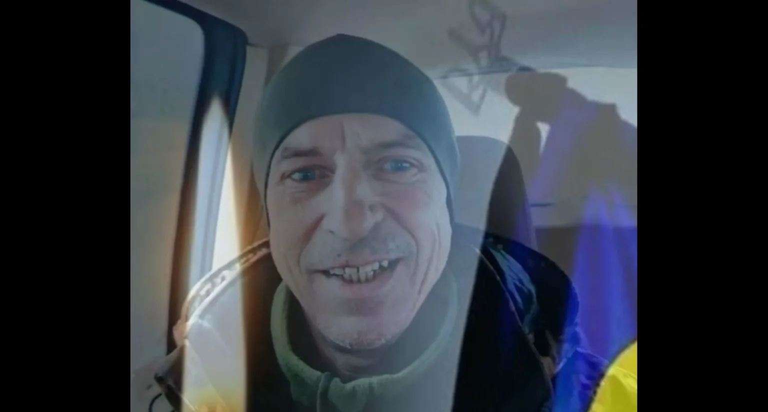 Чоловік у шапці посміхається, сидячи в машині