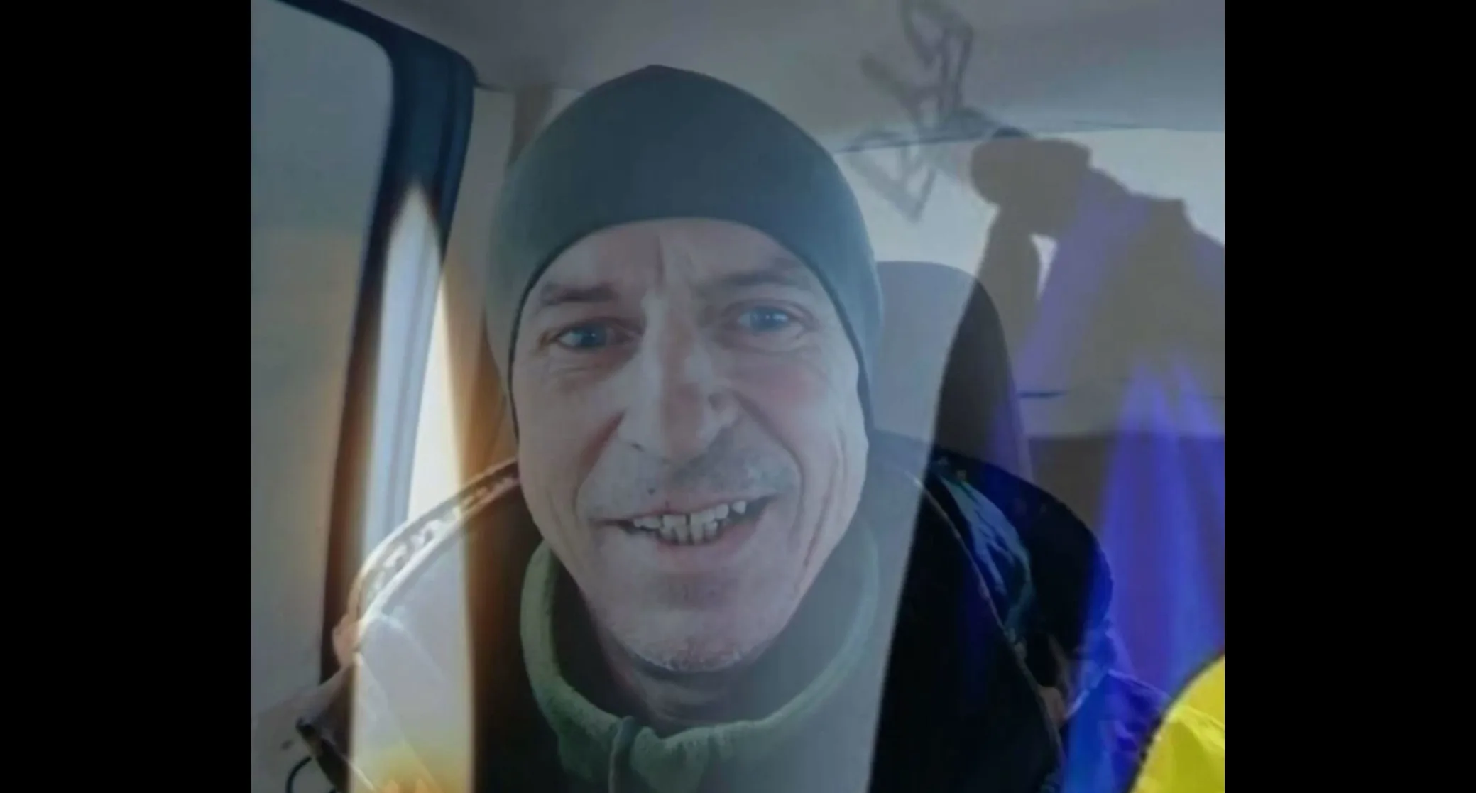 Чоловік у шапці посміхається, сидячи в машині
