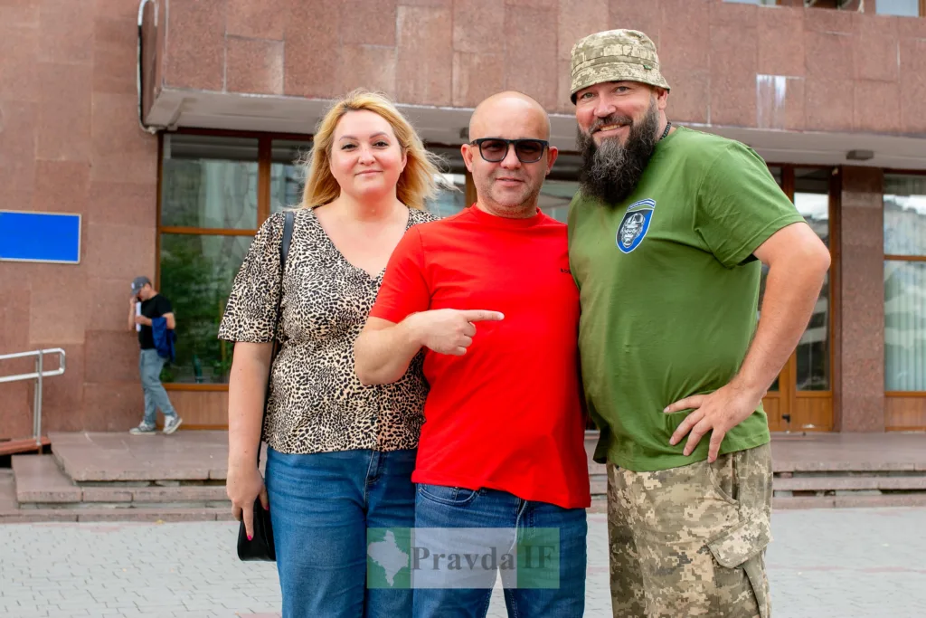 Троє людей позують перед будівлею міста