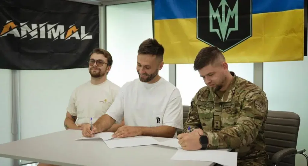 Троє чоловіків підписують документи перед прапорами України