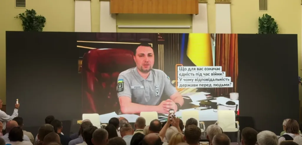Виступ посадовця на великому екрані перед аудиторією