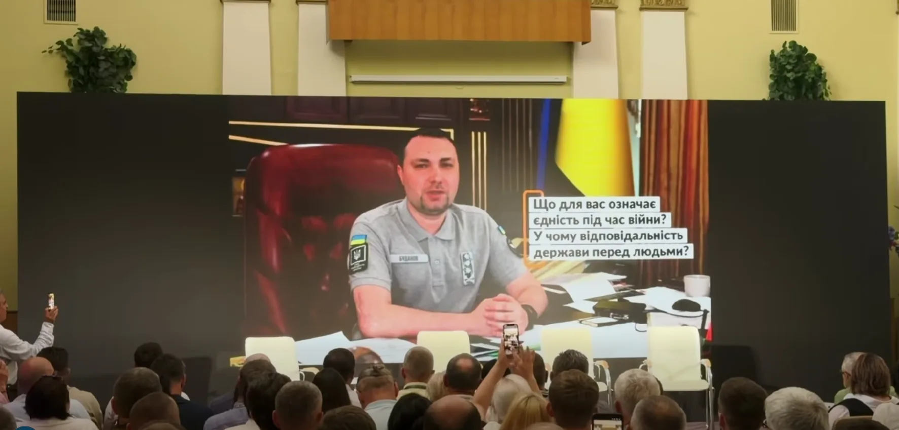 Виступ посадовця на великому екрані перед аудиторією