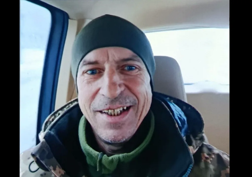 Чоловік у військовому одязі посміхається в машині