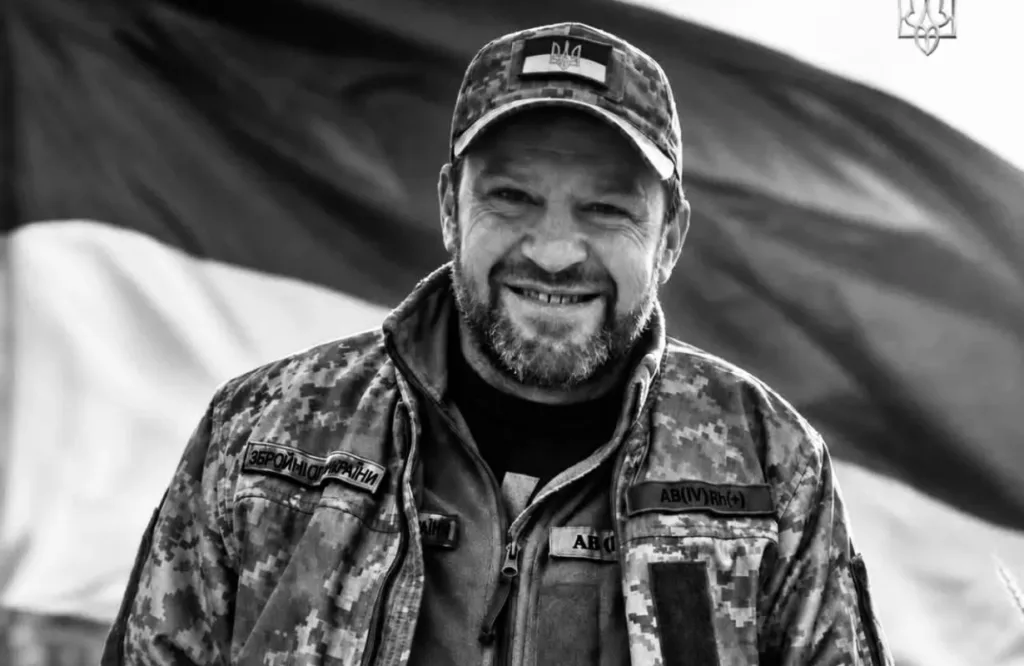 Усміхнений український військовий у камуфляжі на тлі прапора