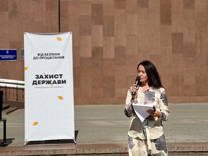 Жінка виступає з мікрофоном біля банера організації
