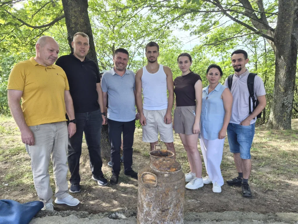 Група людей біля іржавої металевої ємності під деревами