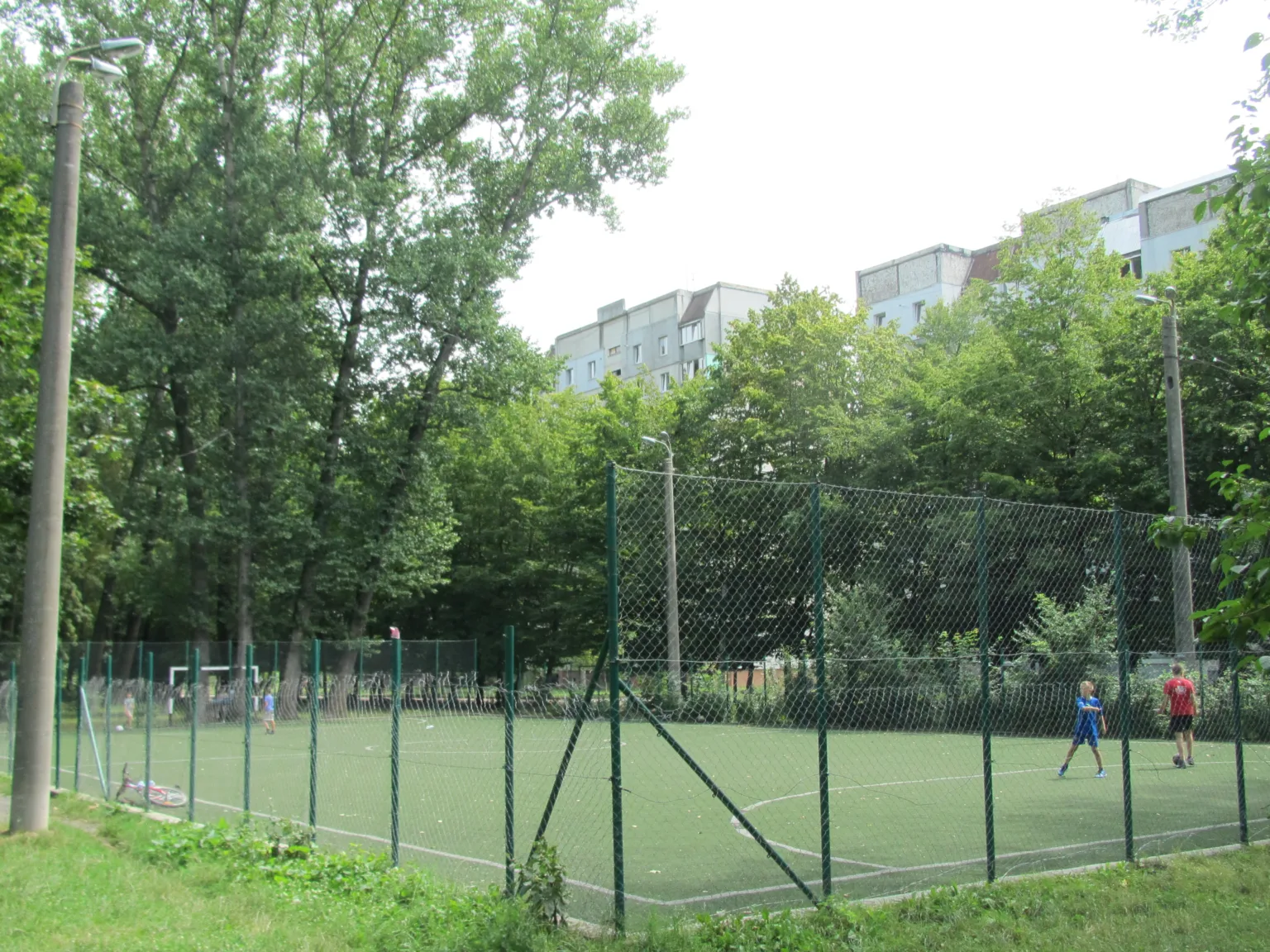 Діти грають на огородженому футбольному майданчику серед дерев