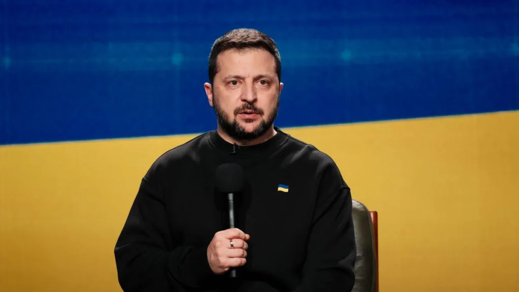 Володимир Зеленський виступає з мікрофоном на тлі прапора України