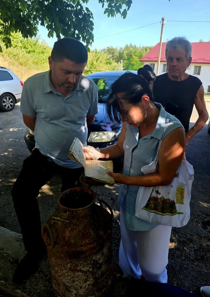 Троє людей розглядають старий записник біля іржавого бідона