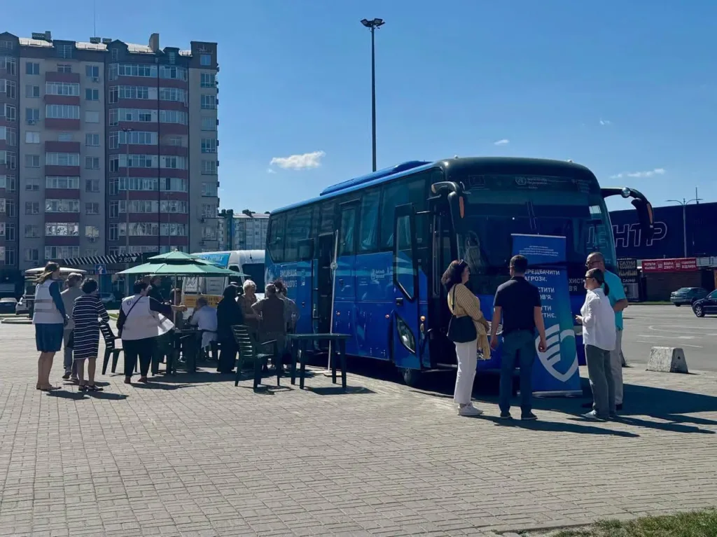Люди біля синього інформаційного автобуса на міській площі