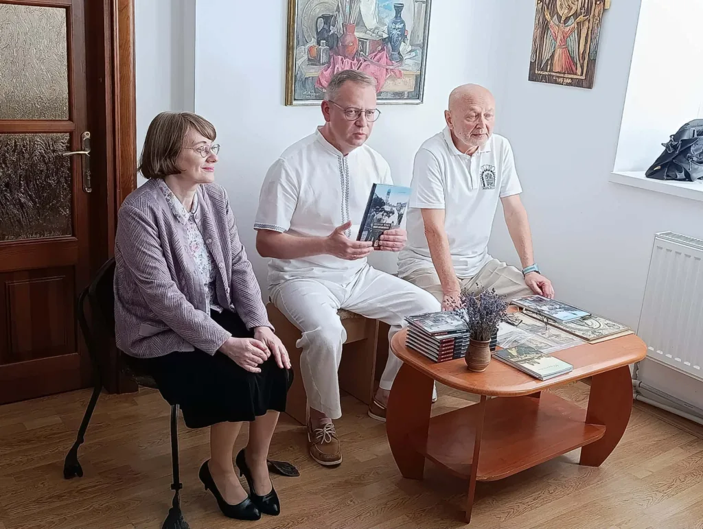 Троє людей презентують книгу в кімнаті з картинами