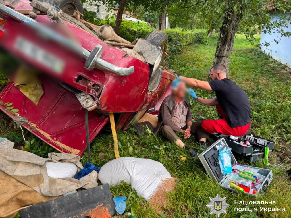 Перекинутий червоний автомобіль і рятувальник біля постраждалого