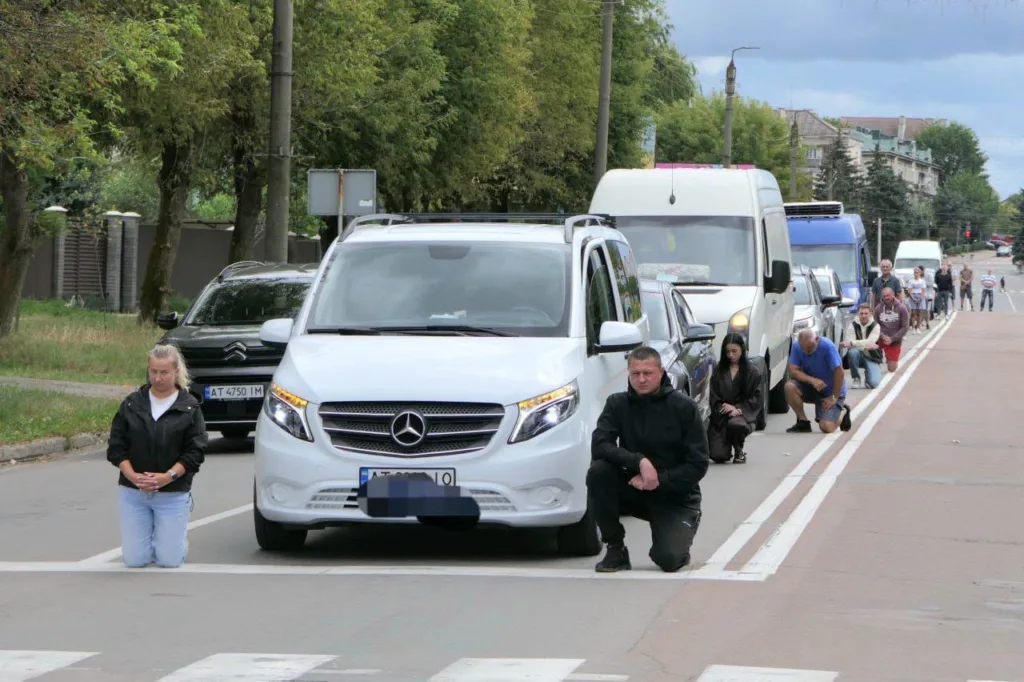 Люди навколішки вздовж колони автомобілів на вулиці