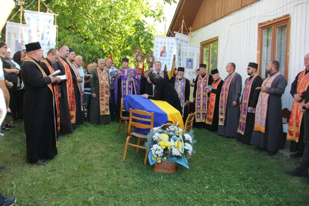 Священники моляться біля труни, вкритої українським прапором
