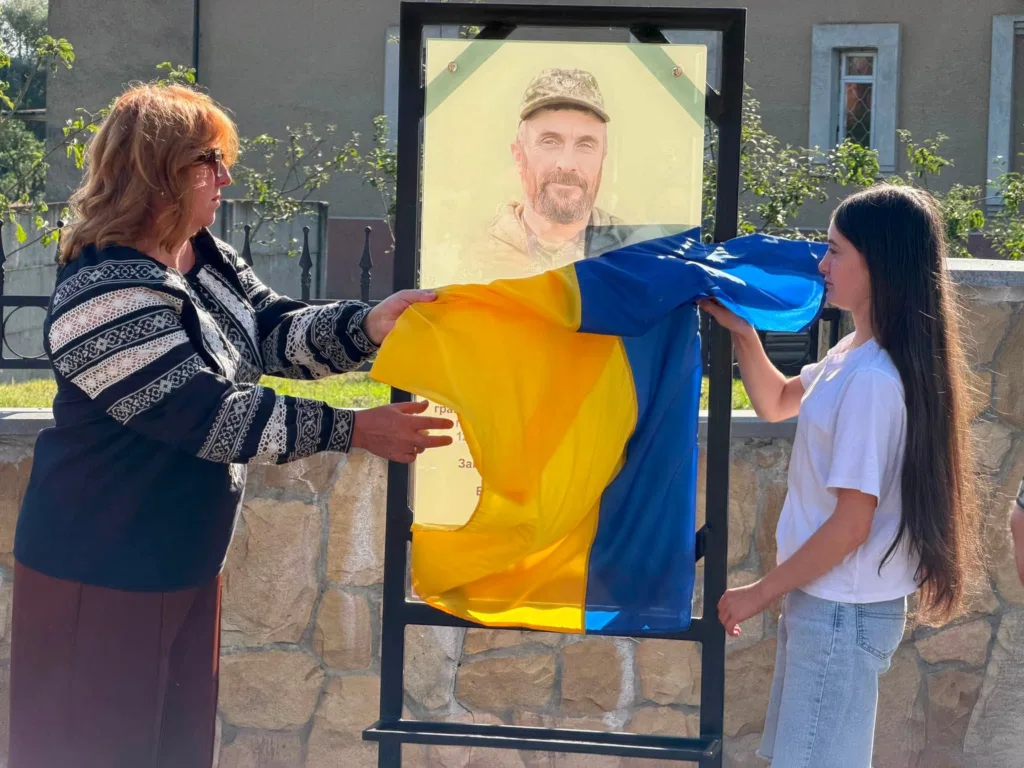 Жінка й дівчина відкривають меморіальну дошку військовому