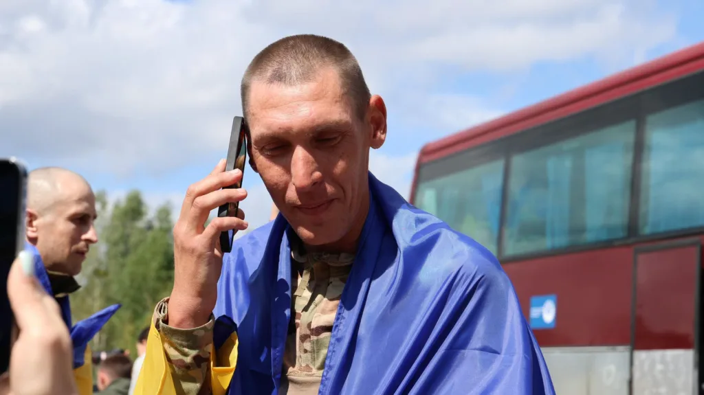 Військовий у прапорі України розмовляє телефоном біля автобуса