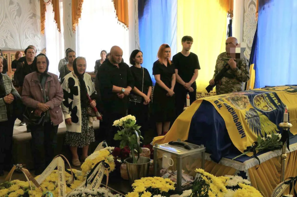 Люди прощаються з військовим біля труни з прапором