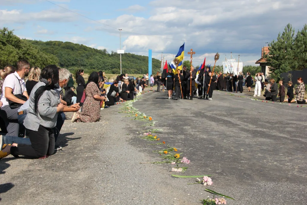 Люди навколішки зустрічають релігійну процесію з українськими прапорами