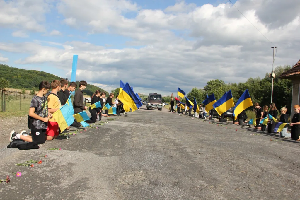 Діти навколішки з українськими прапорами зустрічають кортеж