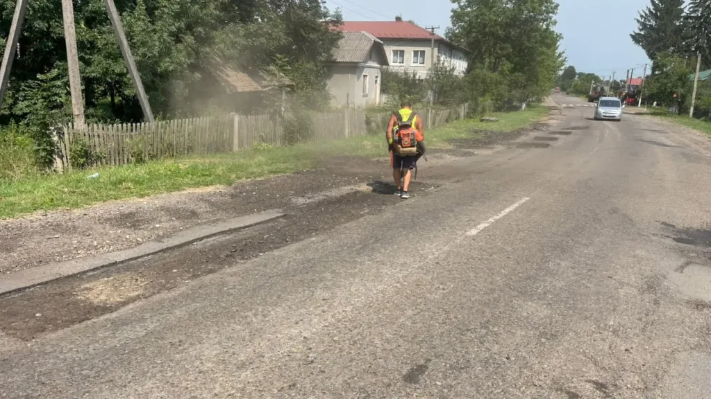 Працівник обкошують узбіччя сільської дороги мотокосою