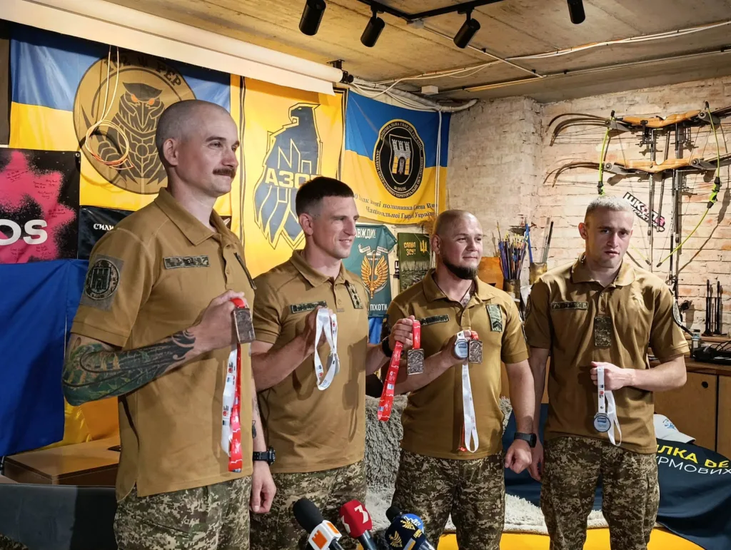 Четверо військових із медалями на тлі прапорів